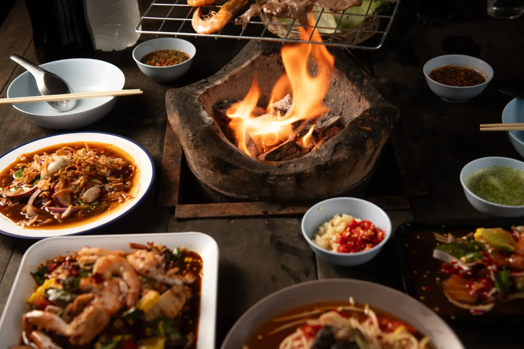 Charcoal grill with flames beside Thai dishes